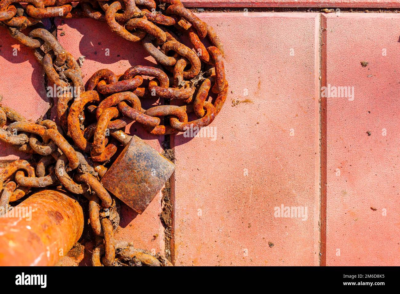 Eine alte rostige Kette und ein Vorhängeschloss, die an einem Pfosten befestigt sind und auf dem Boden liegen. Stockfoto