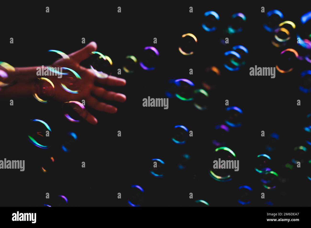 Die Hand versucht, farbenfrohe Blasen vor dunklem Hintergrund zu fangen Stockfoto
