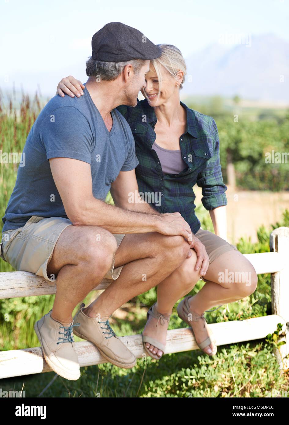 Ländliche Romantik. Ein glückliches, reifes Paar, das zusammen auf einem Zaun sitzt. Stockfoto