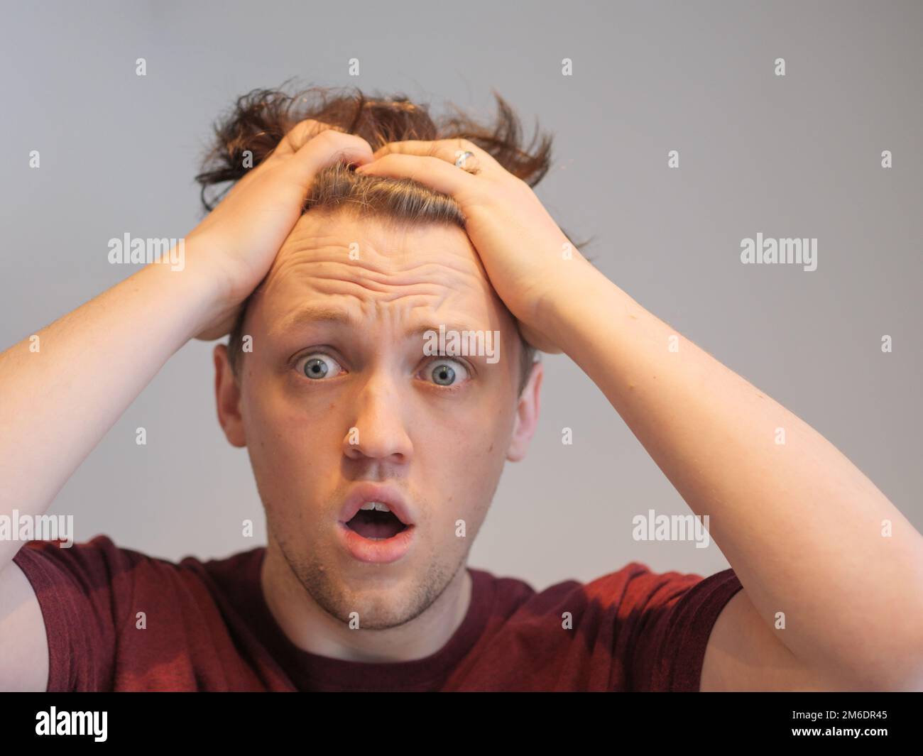 Ein gutaussehender junger Mann, der schockiert mit den Händen auf dem Kopf aussieht Stockfoto
