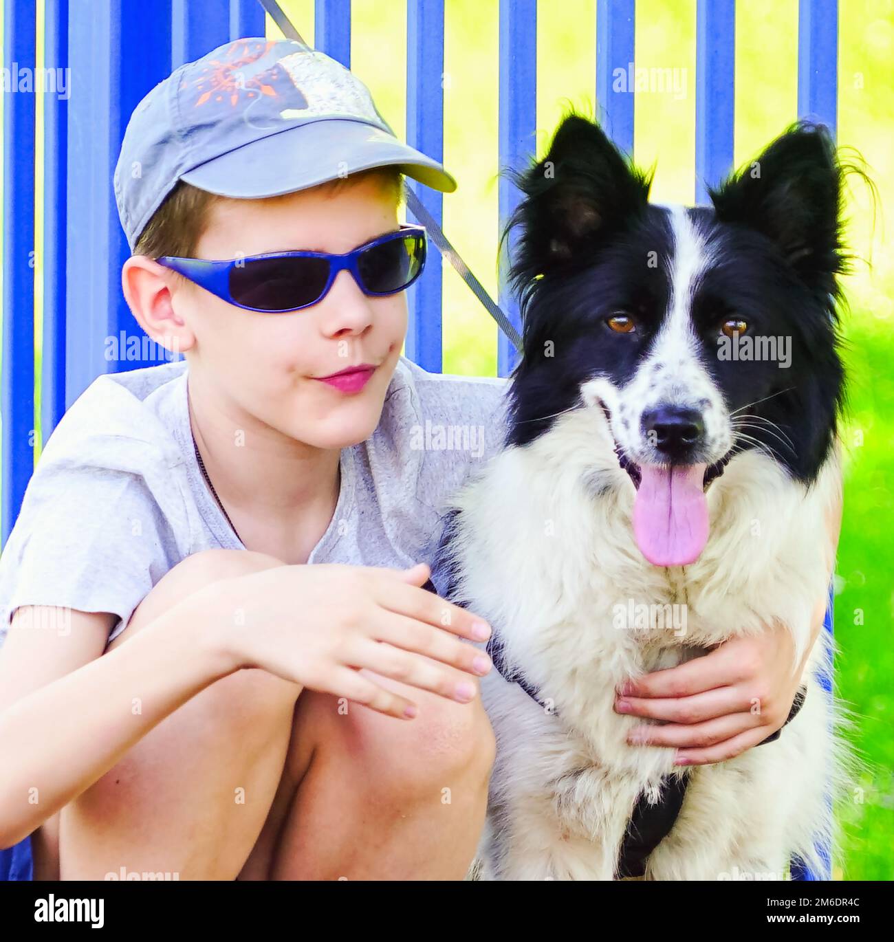 Ein Junge mit dunkler Brille sitzt und umarmt einen Hund. Stockfoto