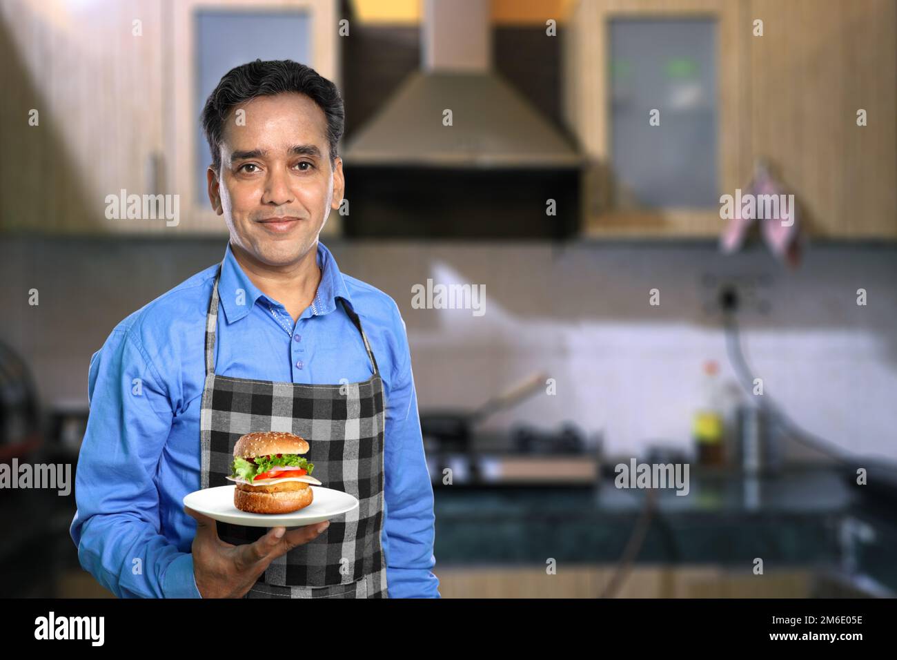 Indischer Küchenchef mit Burger in einer Küche Stockfoto