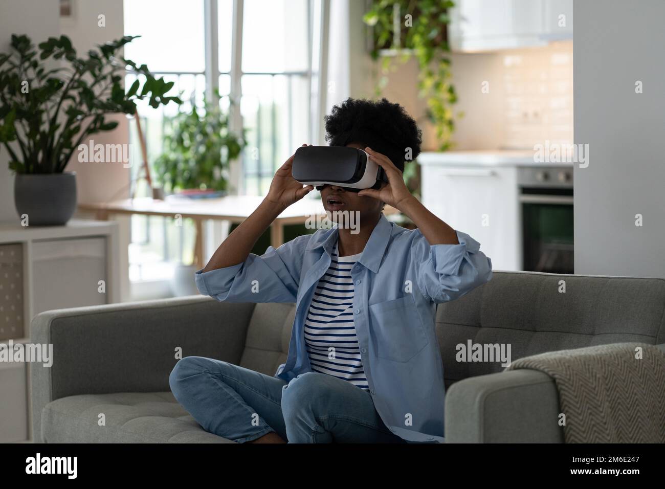 Ermutigte überraschte Frau, die VR-Brillen für Filme mit 3D-Effekt verwendet, die auf dem Sofa zu Hause sitzt Stockfoto