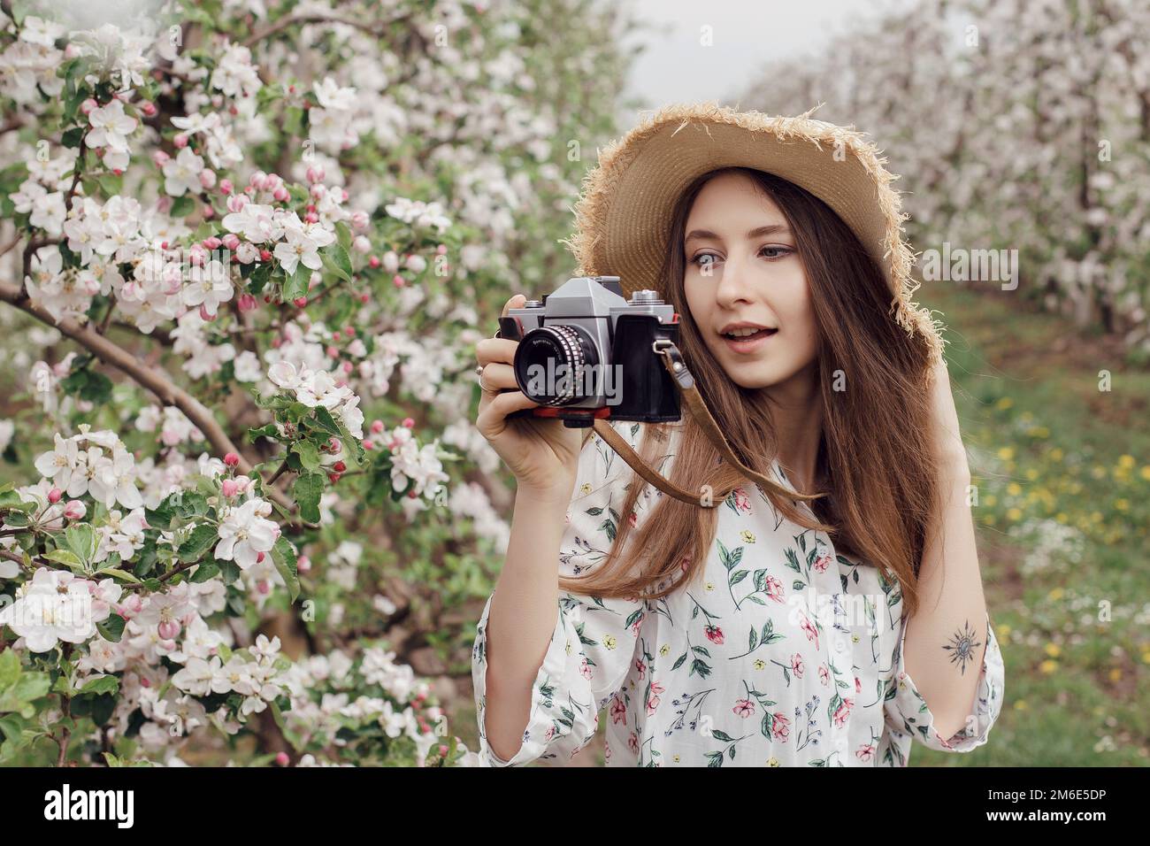 Naturfotograf, der Fotos im Freien macht. Hübsches Mädchen mit Hut und Kleid in einem Apfelgarten. Draußen vor der Stadt. Stockfoto