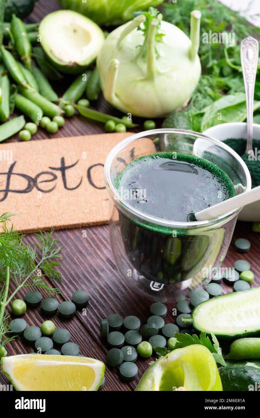 Entgiftungsgrüner Cocktail mit Spirulina um Gemüse. Lifestyle-Konzept. Verschiedene frische grüne Gemüsesorten am Holztisch. Stockfoto