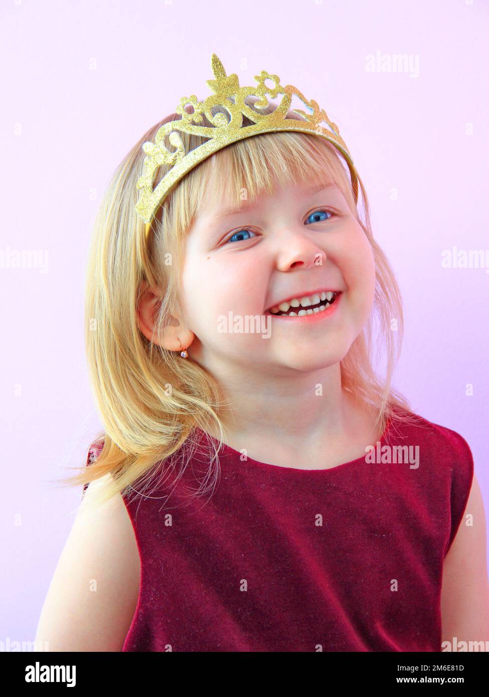 Ein kleines Mädchen mit einer lächelnden Krone auf dem Kopf. Ein Kind in einem schönen Kleid, das lacht. Das kleine Mädchen lächelt Stockfoto