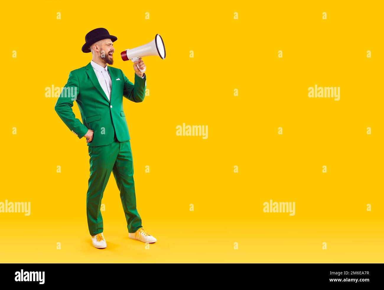 Mann im grünen Anzug macht Durchsage durch Megafon auf gelbem Hintergrund Stockfoto