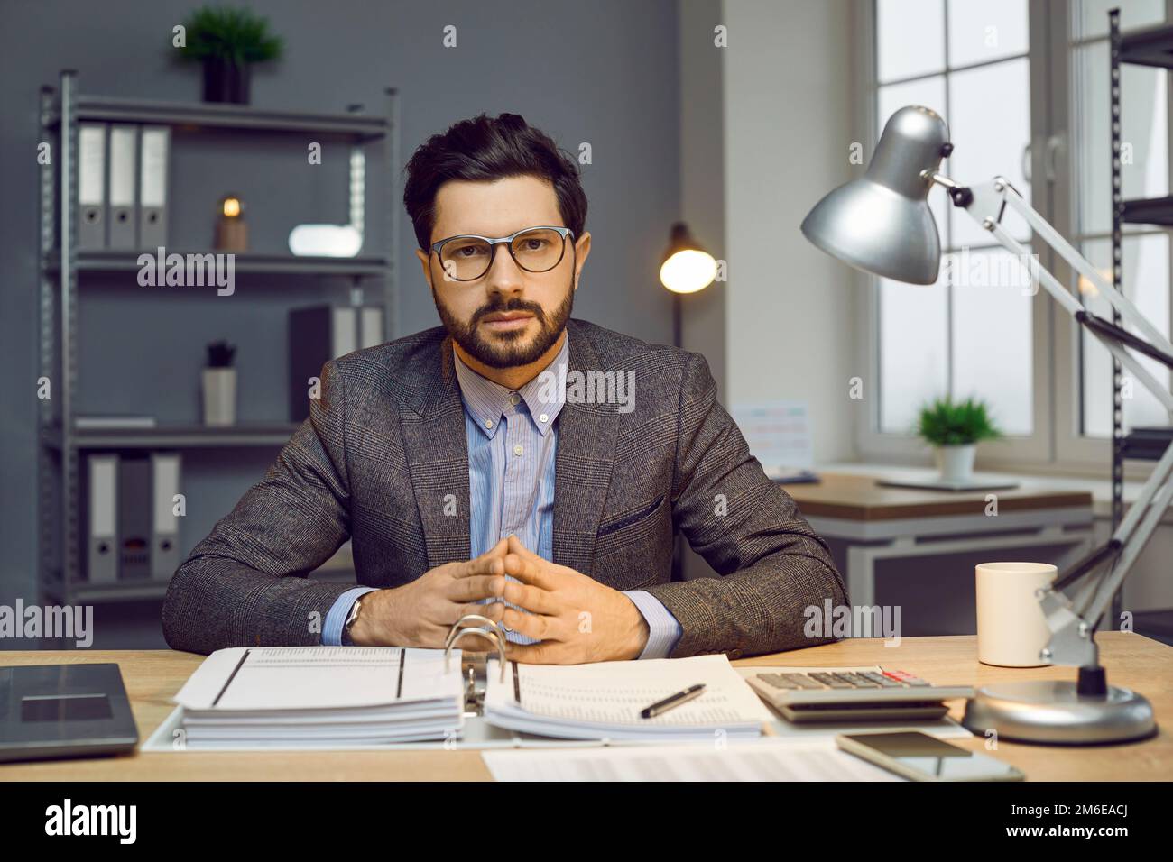 Seriöser selbstbewusster Geschäftsmann, der in einem modernen Büro am Schreibtisch sitzt Stockfoto