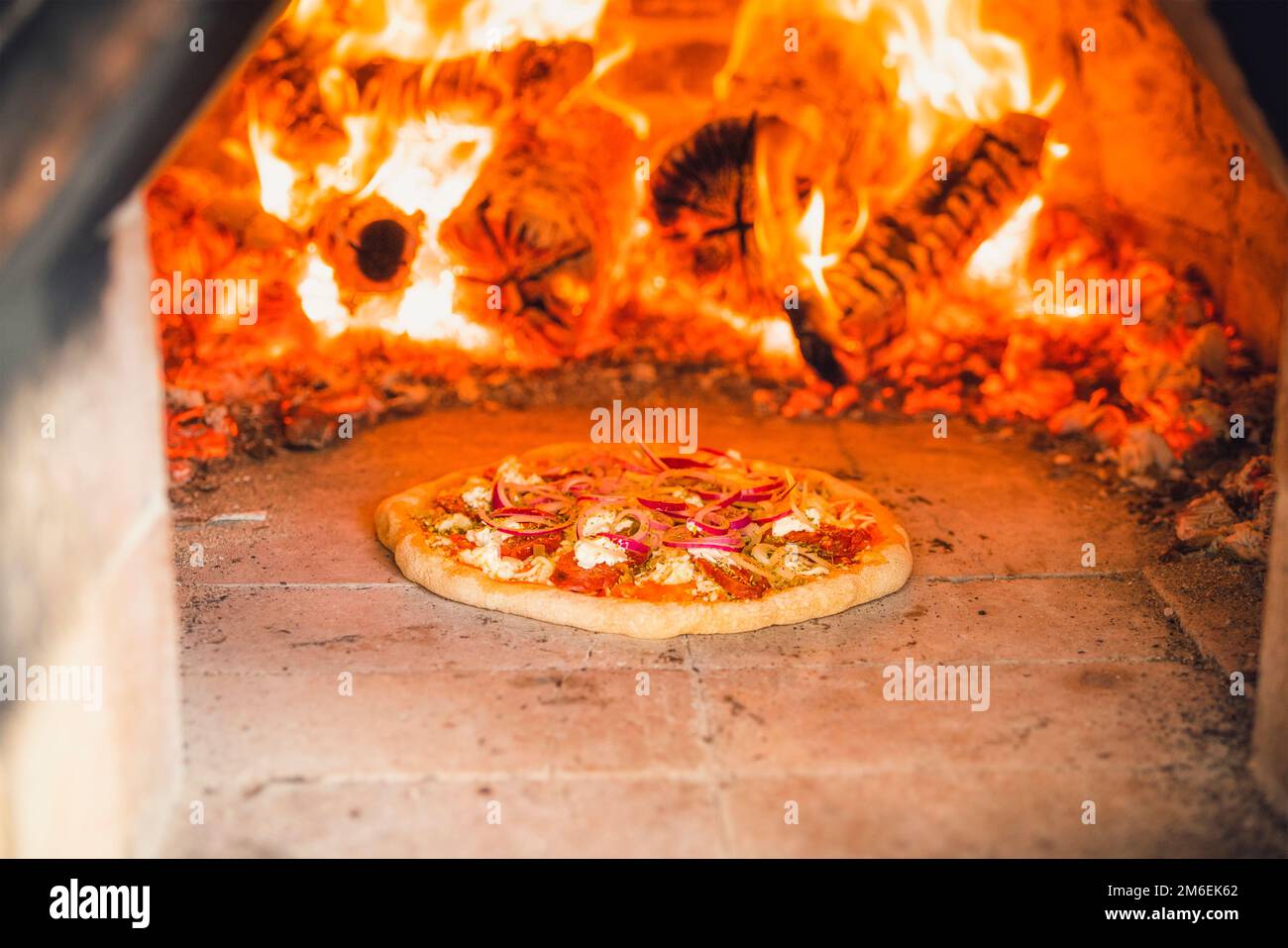 Pizza mit Belag in einem heißen Steinofen mit Feuerholz, das eine köstliche Mahlzeit backt Stockfoto