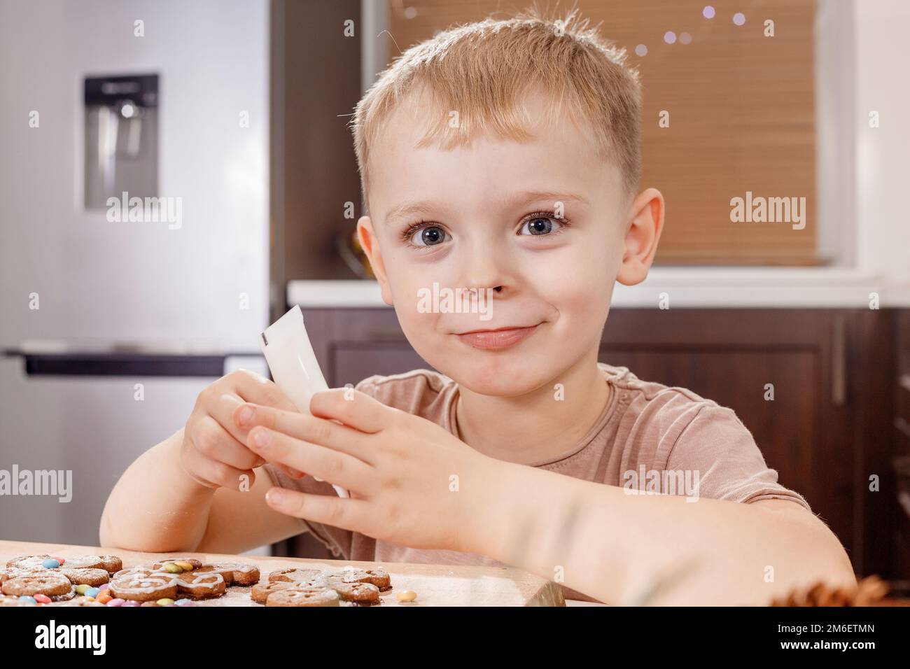 Ein kleiner Junge, der Lebkuchen malt. Handgefertigte Geschenkideen für Weihnachten. Küche zu Weihnachten dekoriert. Horizontale Aufnahme. Stockfoto