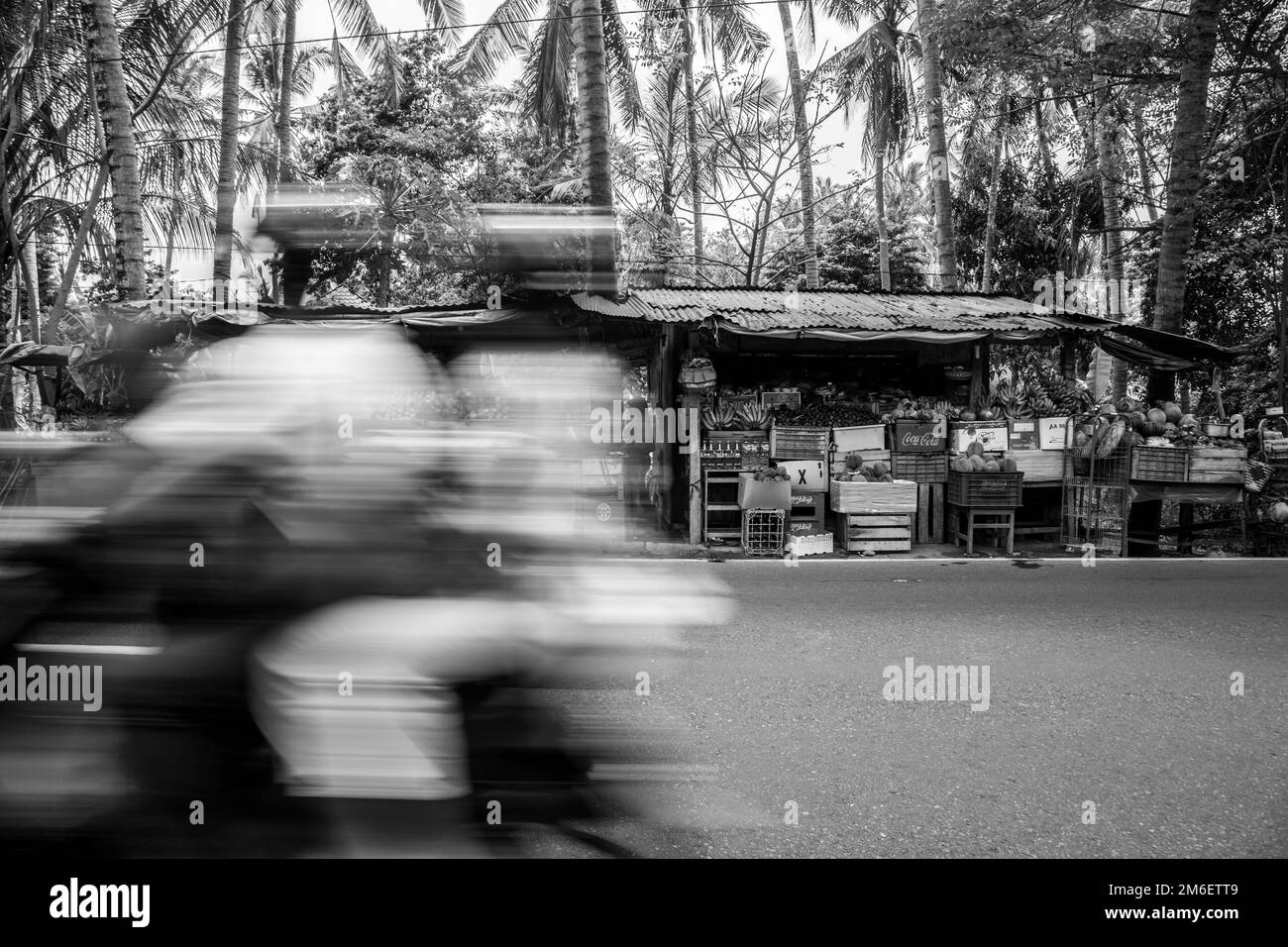Schwarzweißfoto eines Straßenverkäufers im Hintergrund, aufgenommen, während eine Familie mit einem Roller im Vordergrund zu schnell fuhr. Indonesien Stockfoto