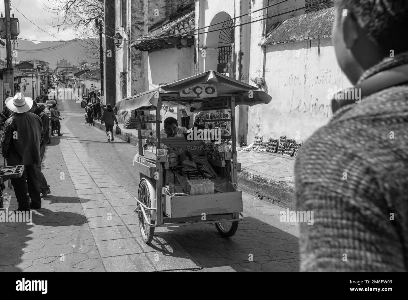 Schwarzweißfoto eines Straßenverkäufers in Mexiko, aufgenommen, während ein zufälliger Mann die Straße überquert. Oaxaca. Stockfoto