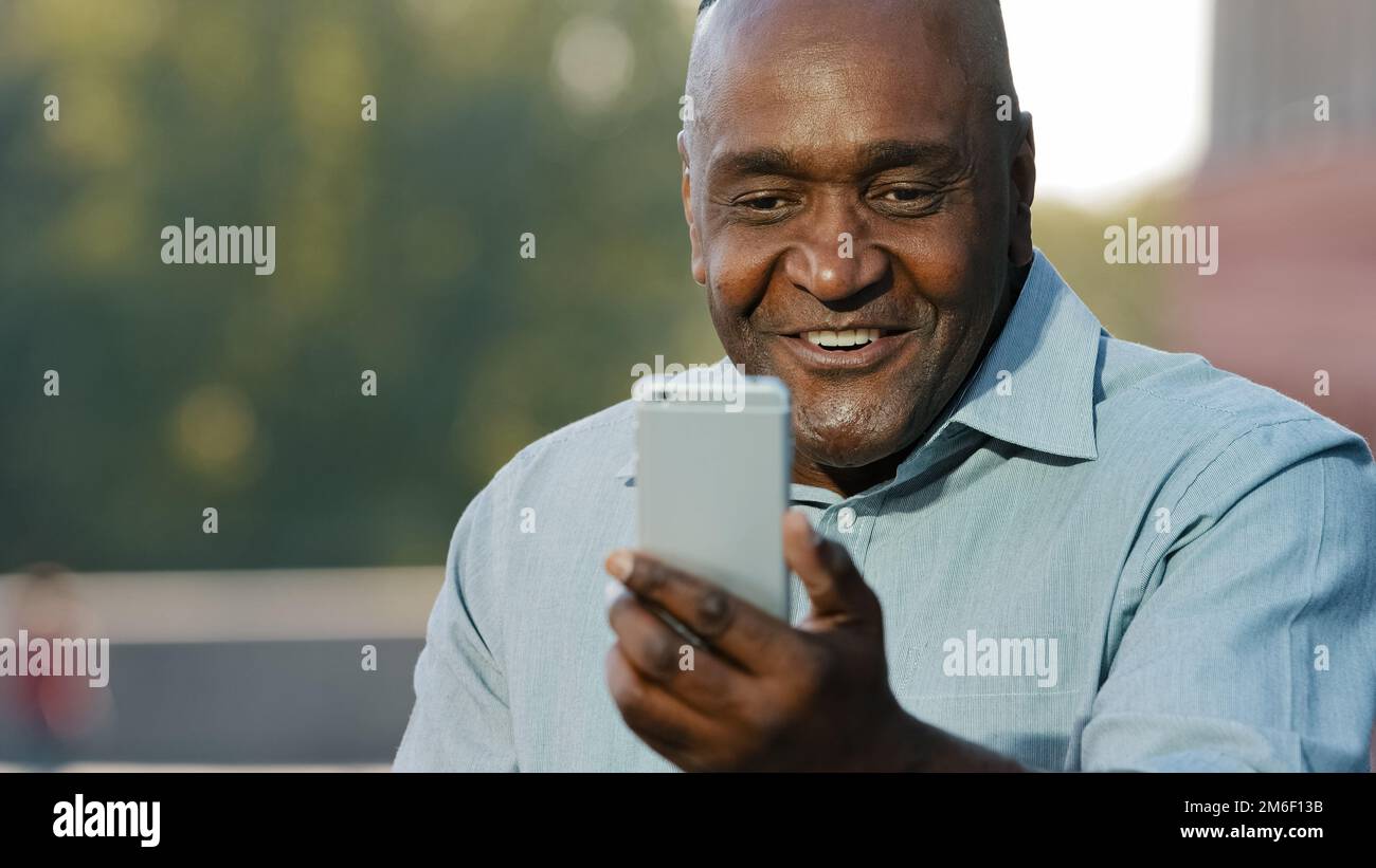 Ein gefühlsmäßiger, afroamerikanischer Mann, der Videoanrufe tätigt und auf eine Smartphone-Kamera schaut, der im Freien in der Stadt mit dem Handy spricht. Ethnisch männlich glücklich erwachsen Stockfoto