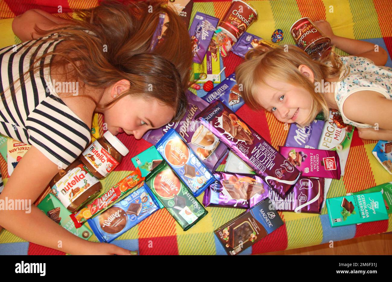 Glückliche Kinder liegen in einem Haufen Süßigkeiten und Schokolade. Kinder amüsieren sich Stockfoto