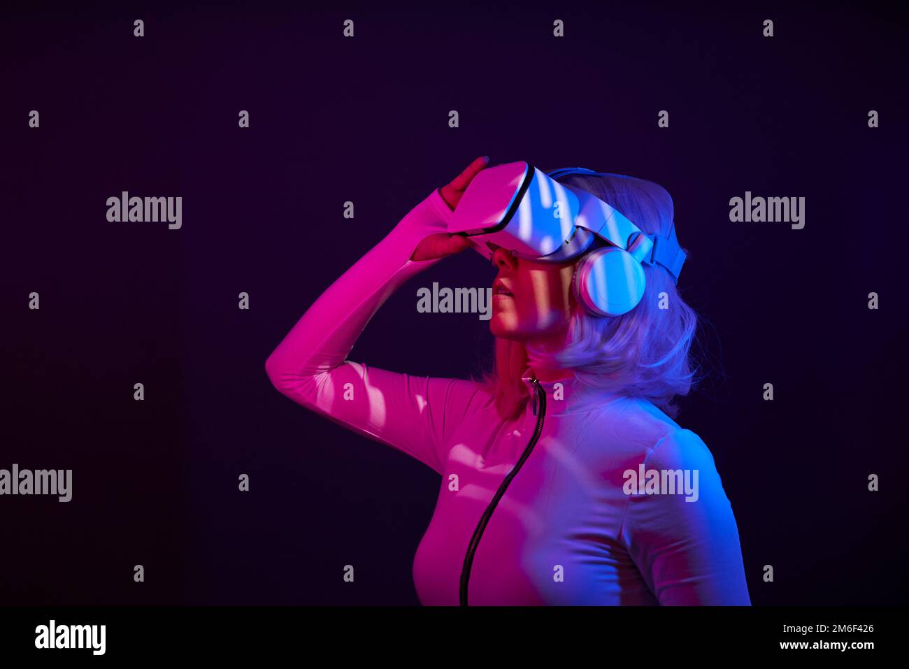 Eine Frau in Virtual-Reality-Brille in Neonfarben. Das Konzept der digitalen Technologie für Metaversum und Unterhaltung der Zukunft. Stockfoto
