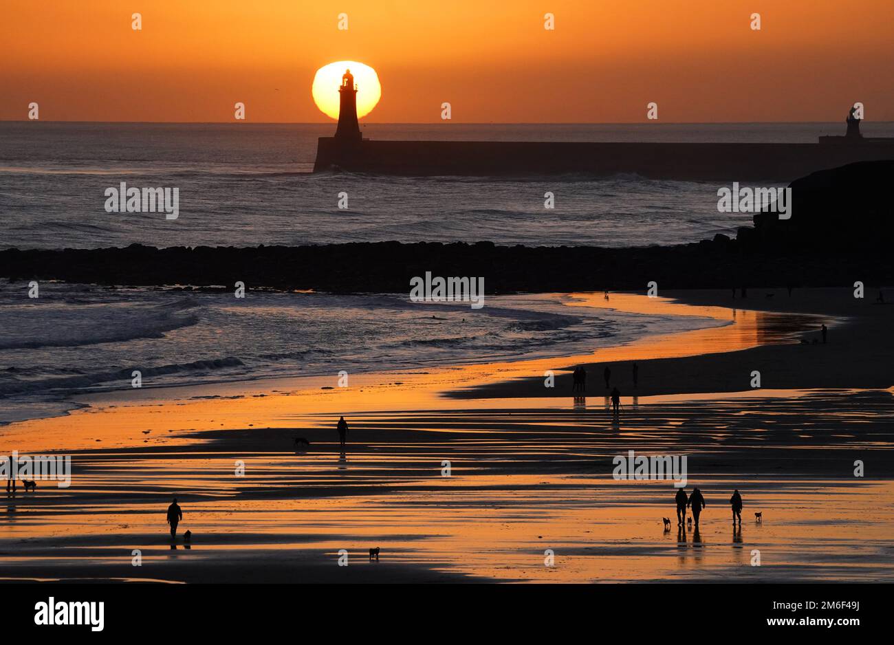 Datei Foto vom 24/12/22 von Menschen, die bei Sonnenaufgang am Tynemouth Longsands Beach im Nordosten Englands laufen, als Küstenstädte seit der Pandemie gedeihen, während sich die Stadtzentren ausgedünnt haben, da sich die Arbeitsmuster für immer verändert haben, neue Mobiltelefondaten deuten darauf hin. Stockfoto