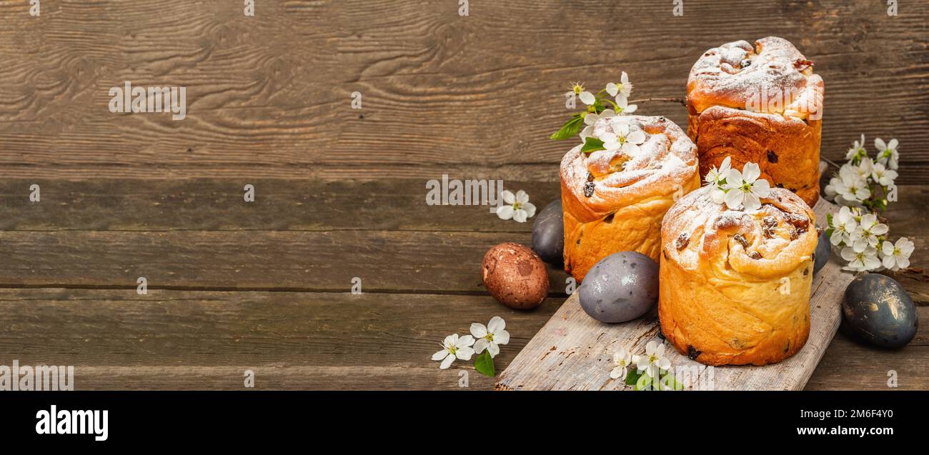 Osterkuchen Cruffin oder süßes Brot kulich mit bemalten Eiern. Traditionelles festliches Backen und frische Kirschblumen, festlicher Holzhintergrund. Jahrgang b Stockfoto