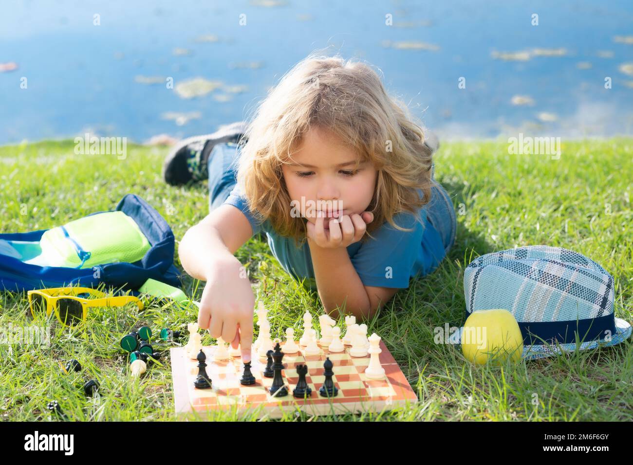 Kleiner Junge spielt Schach im Park. Ein Junge, der draußen Brettspiele spielt. Denk-Kind-Brainstorming und Idee im Schachspiel. Stockfoto
