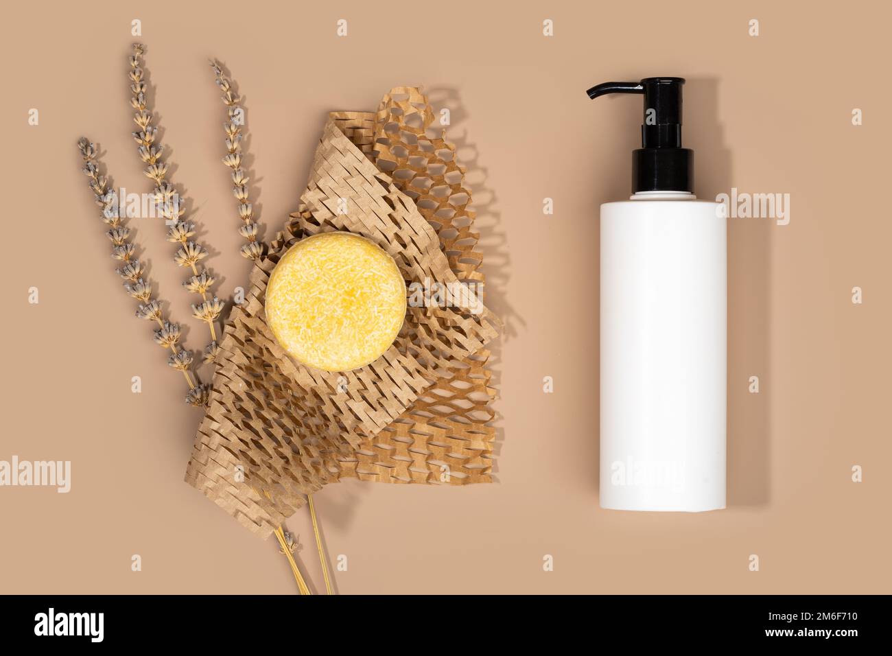Vergleich eines massiven Shampoo-Stabes in einem Wabenpapier mit einem flüssigen Shampoo. Beiger Hintergrund. Nachhaltige Haarpflege. Null Verschwendung Stockfoto