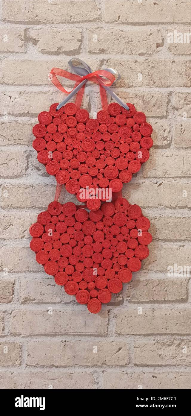 Rote Herzen hängen an einer Ziegelwand. Strukturiertes Symbol der Liebe. Zwei handgemachte Herzen an einer hellen Ziegelwand Stockfoto