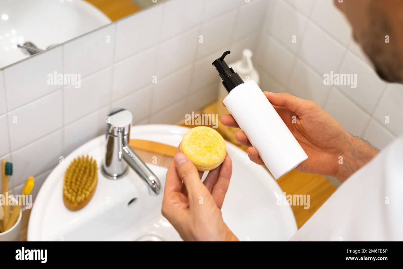 Der Mann hat die Wahl zwischen einem festen Shampoo-Riegel und einem flüssigen. Plastikfrei, kein Abfall, geringe Wassermenge. Nachhaltige Haarpflege. Badezimmer Stockfoto