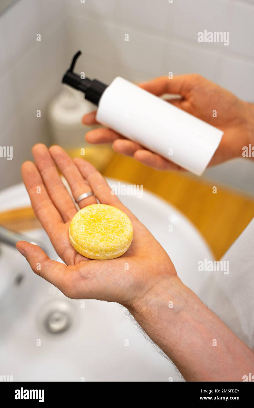 Der Mann hat die Wahl zwischen einem festen Shampoo-Riegel und einem flüssigen. Badezimmerzubehör. Nachhaltige Haarpflege. Ohne Plastik, ohne Abfall, wenig Abfall Stockfoto