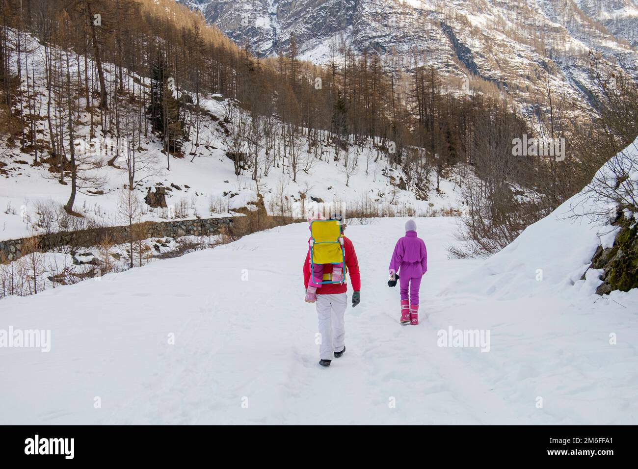 Mann und Frau mit einem Baby in einem Rucksackträger, die auf dem Feld in einer verschneiten Berglandschaft spazieren Stockfoto