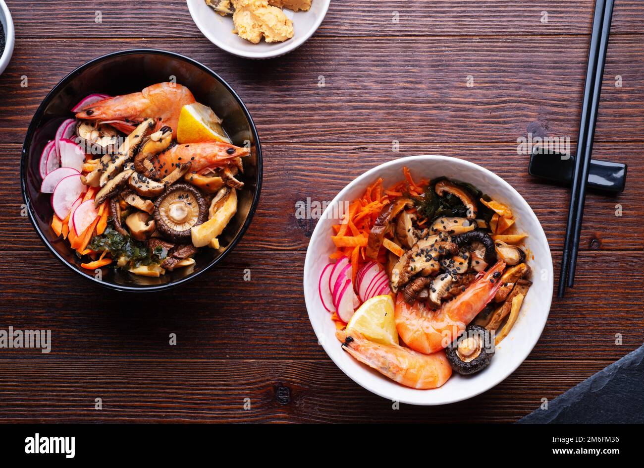 Miso Suppe mit Muscheln, Garnelen, Shiitake-Pilzen und Gemüse. Serviert an einem dunkelbraunen Holztisch. Flach verlegt Stockfoto