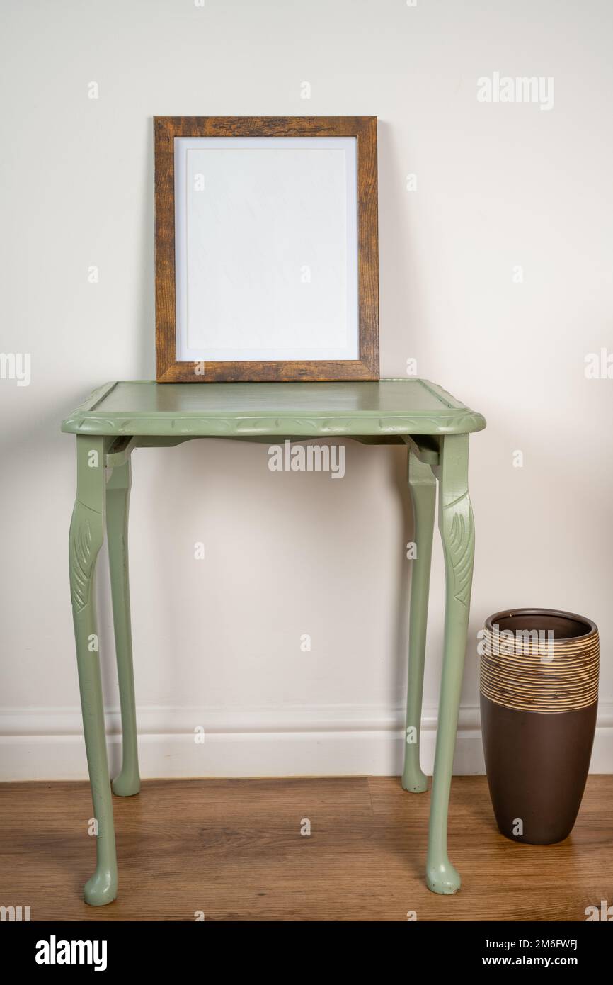Bilderrahmen auf einem grünen Tisch vor einem sauberen Wandhintergrund und Holzboden mit Keramikvase Stockfoto