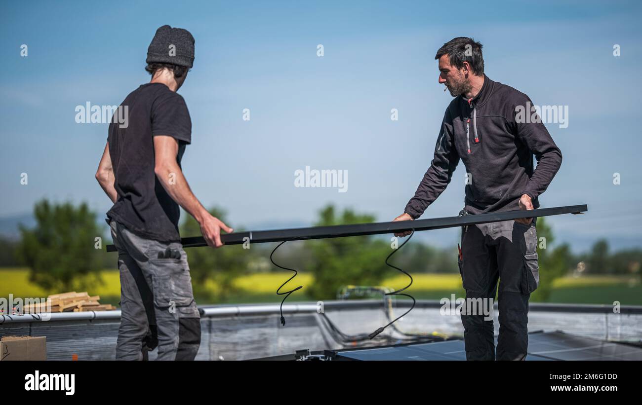 Männliche Teamingenieure, die eigenständige Solarpaneele installieren. Elektriker montieren blaues Solarmodul auf dem Dach des Unternehmens. Alternative en Stockfoto