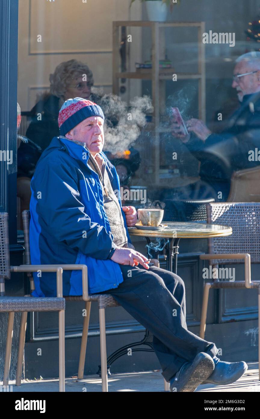 Ausatmen von Zigarettenrauch bei eiskaltem Winterwetter bei einer Tasse Kaffee in einem Café in Henley-upon-Thames, Oxfordshire, Großbritannien. Stockfoto