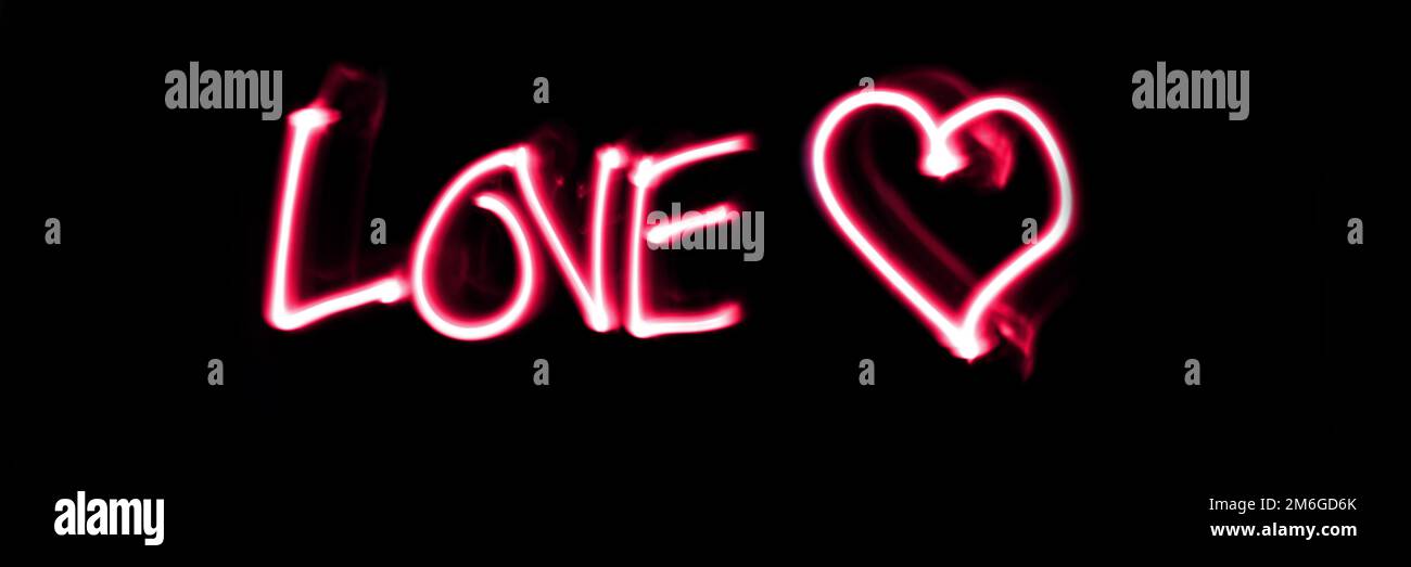 Das Wort liebt weiß ein Herz in Pink auf schwarzem Panoramaklickgrund. Valentinstag, liebe helle Malerei. Stockfoto