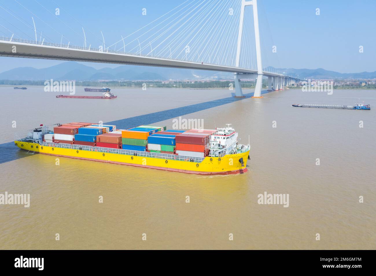 Containerschiff, das auf dem Binnenfluss unter einer Seilbahnbrücke fährt Stockfoto