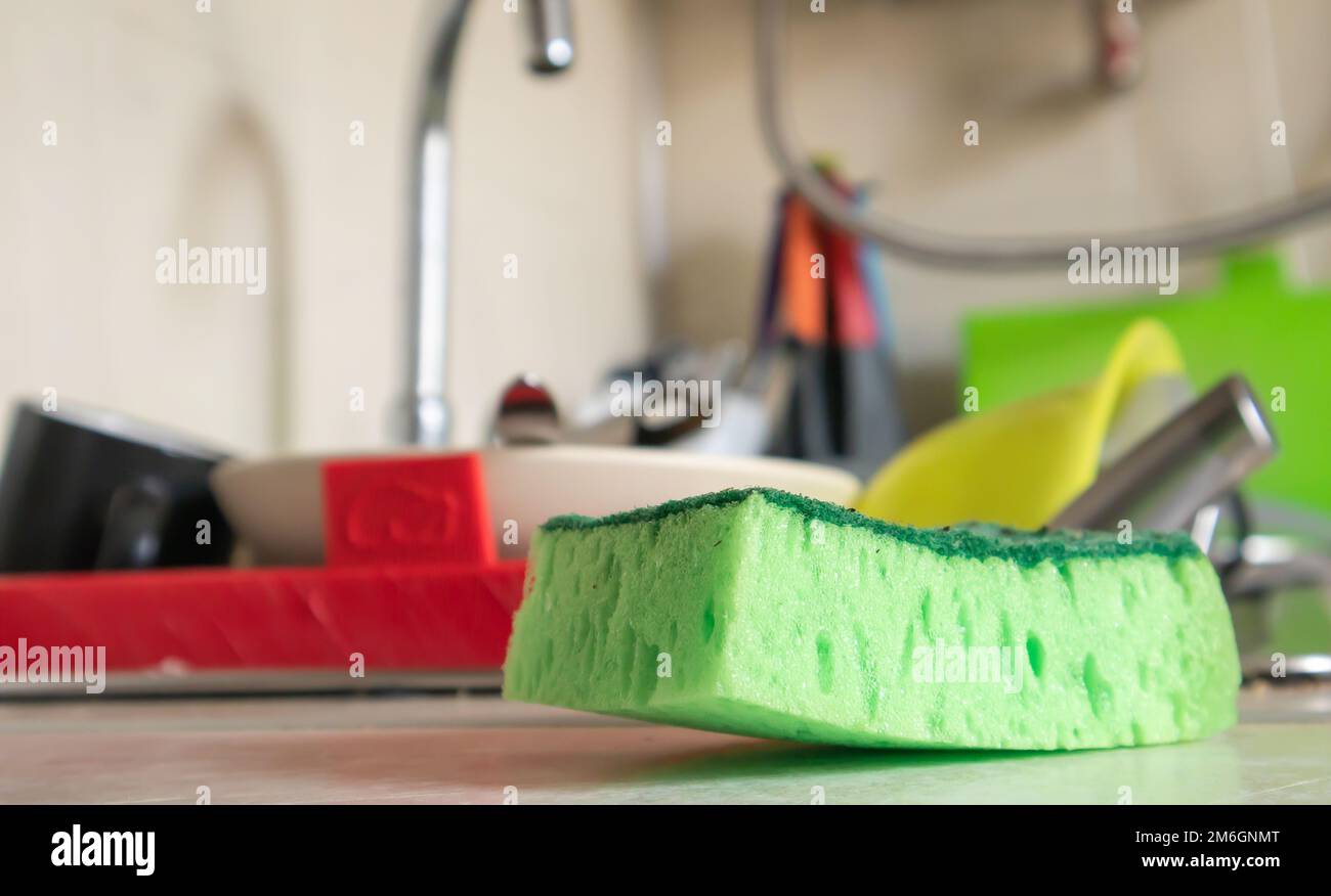 Grüner Schwamm- und Flüssigseifenspender zum Abwaschen von Geschirr auf einem dreckigen Spülbecken komplett mit Geschirr und Küchenutensilien. Waschen d Stockfoto