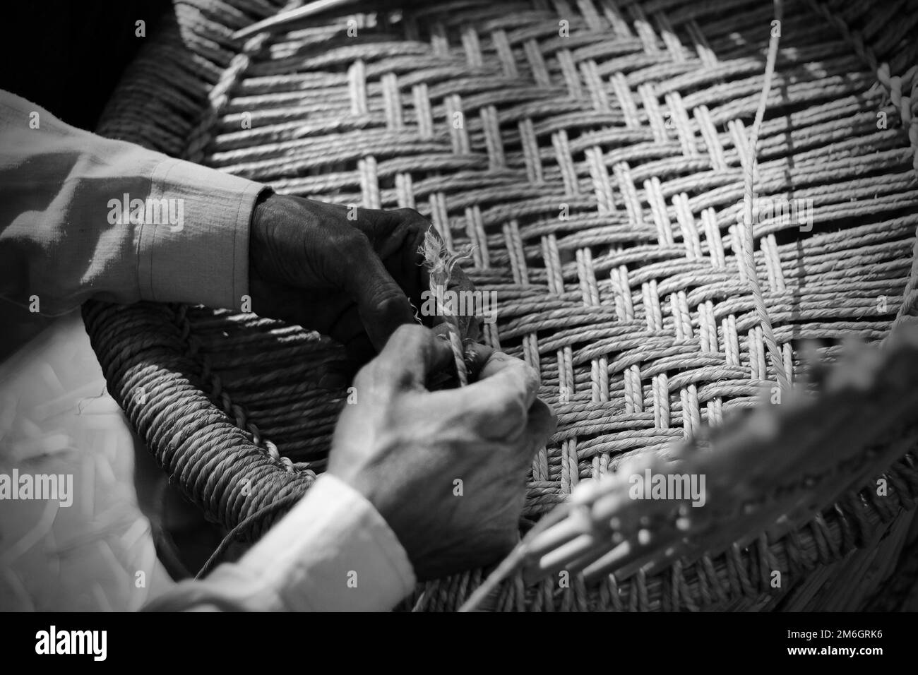 Erfahrener Handwerker, der mit seinen Fingern und Werkzeugen manuell einen detaillierten Bambusholzsessel arbeitet Stockfoto