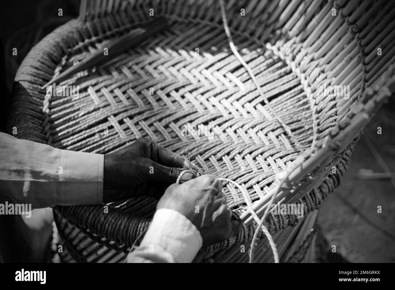 Erfahrener Handwerker, der mit seinen Fingern und Werkzeugen manuell einen detaillierten Bambusholzsessel arbeitet Stockfoto