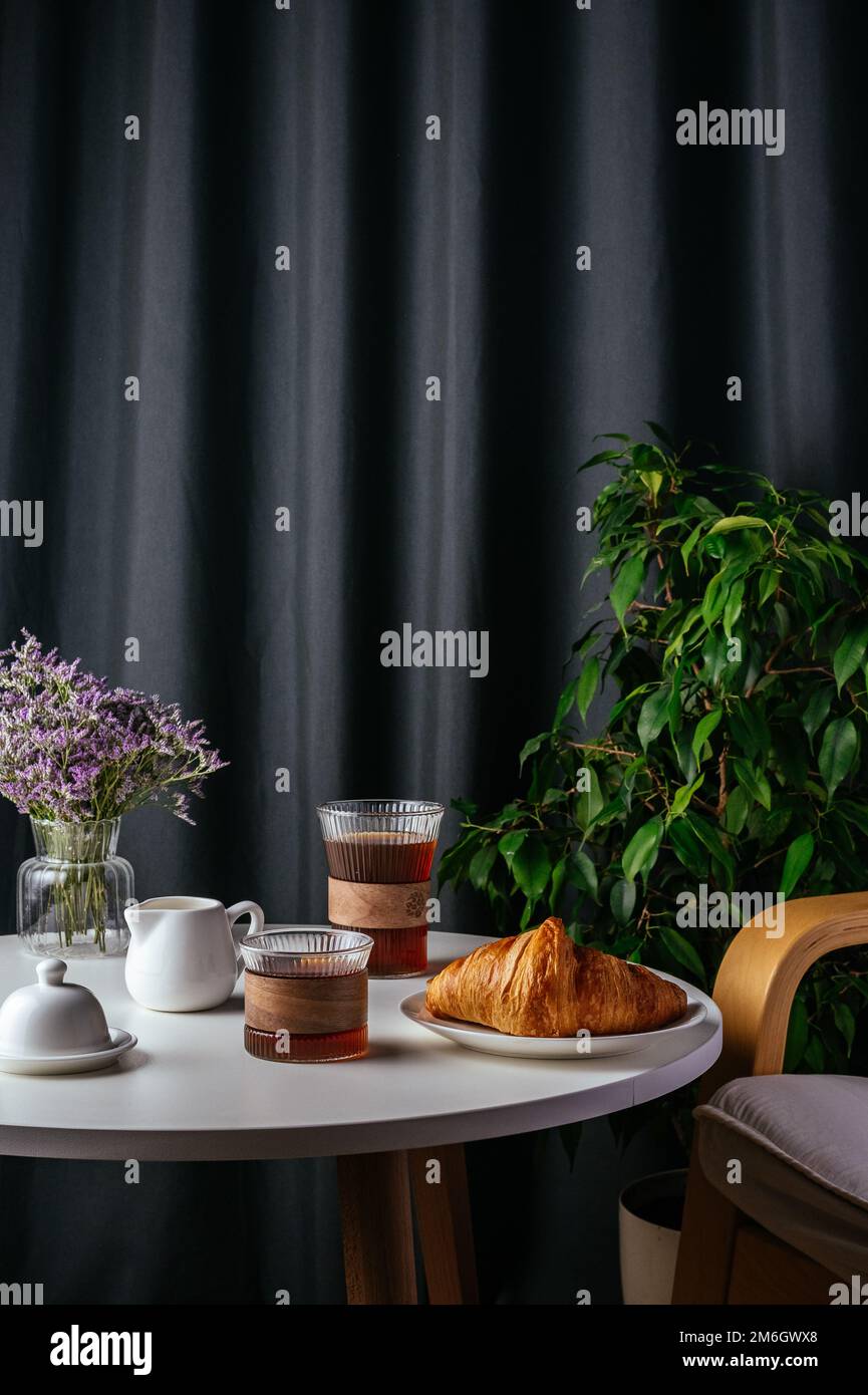 Kaffee und Croissant auf einem Teller auf einem weißen Tisch im Wohnzimmer Stockfoto