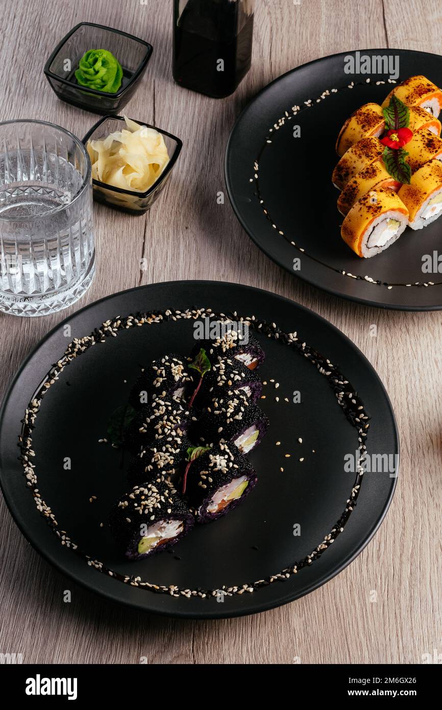 Verschiedene Arten von Sushi-Rollen in Tellern auf dem Tisch. sojasoße, Stockfoto