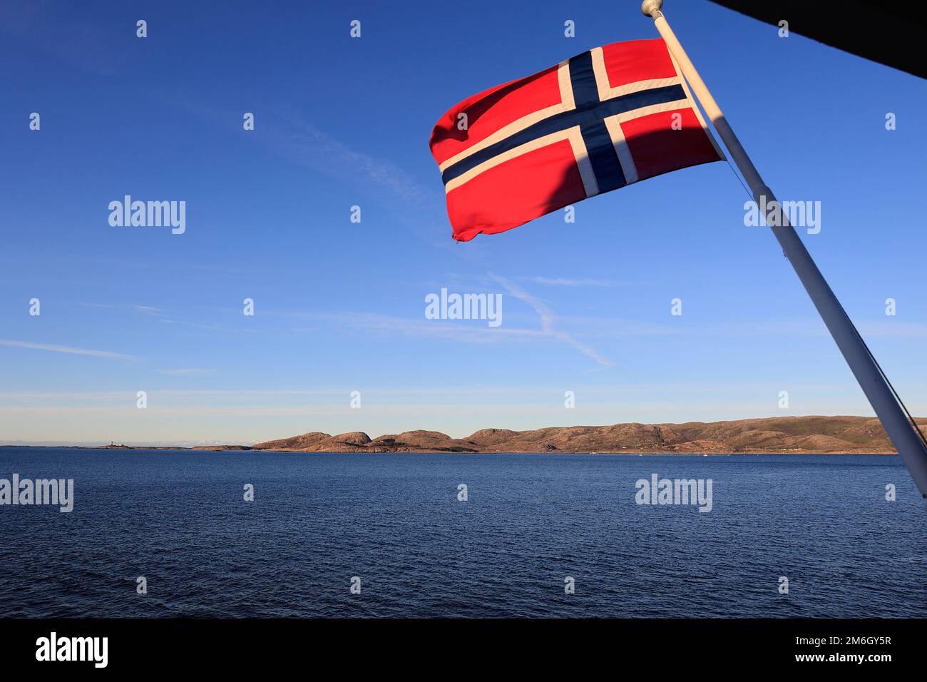 Die Flagge Norwegens, die im Wind auf dem Heck eines Schiffes vor einem blauen Himmel winkt Stockfoto