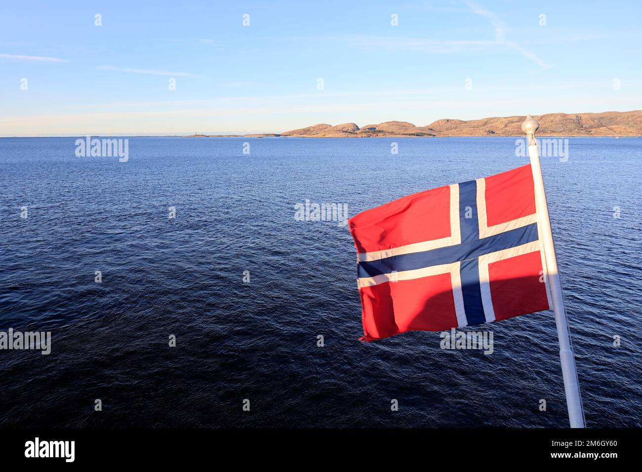 Die Flagge Norwegens, die im Wind auf dem Heck eines Schiffes vor einem blauen Himmel winkt Stockfoto