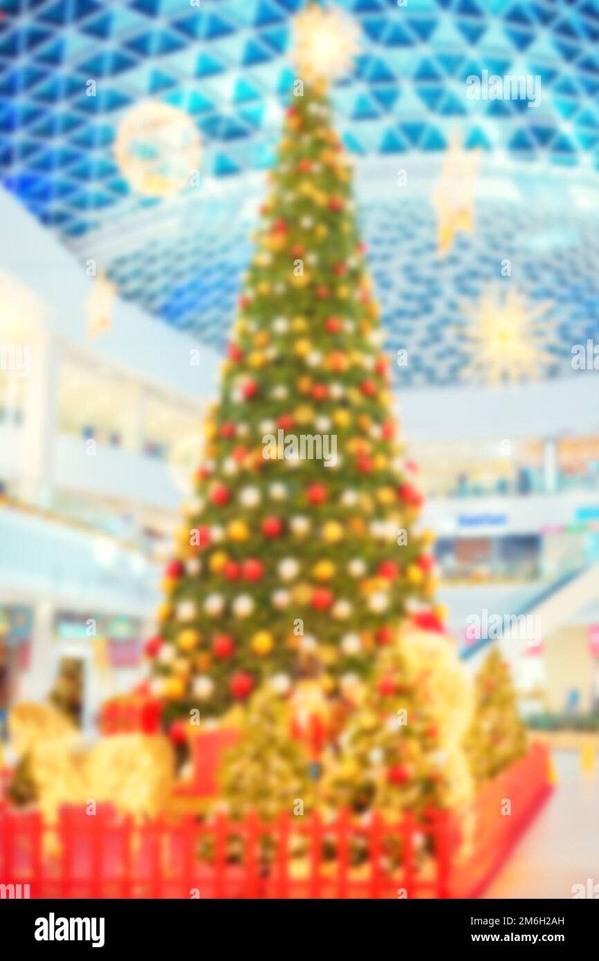 Ein unscharfes Bild eines großen, verkleideten Weihnachtsbaums in der Lobby eines Einkaufszentrums. Vorweihnachtsatmosphäre. Verschwommener Hintergrund Stockfoto