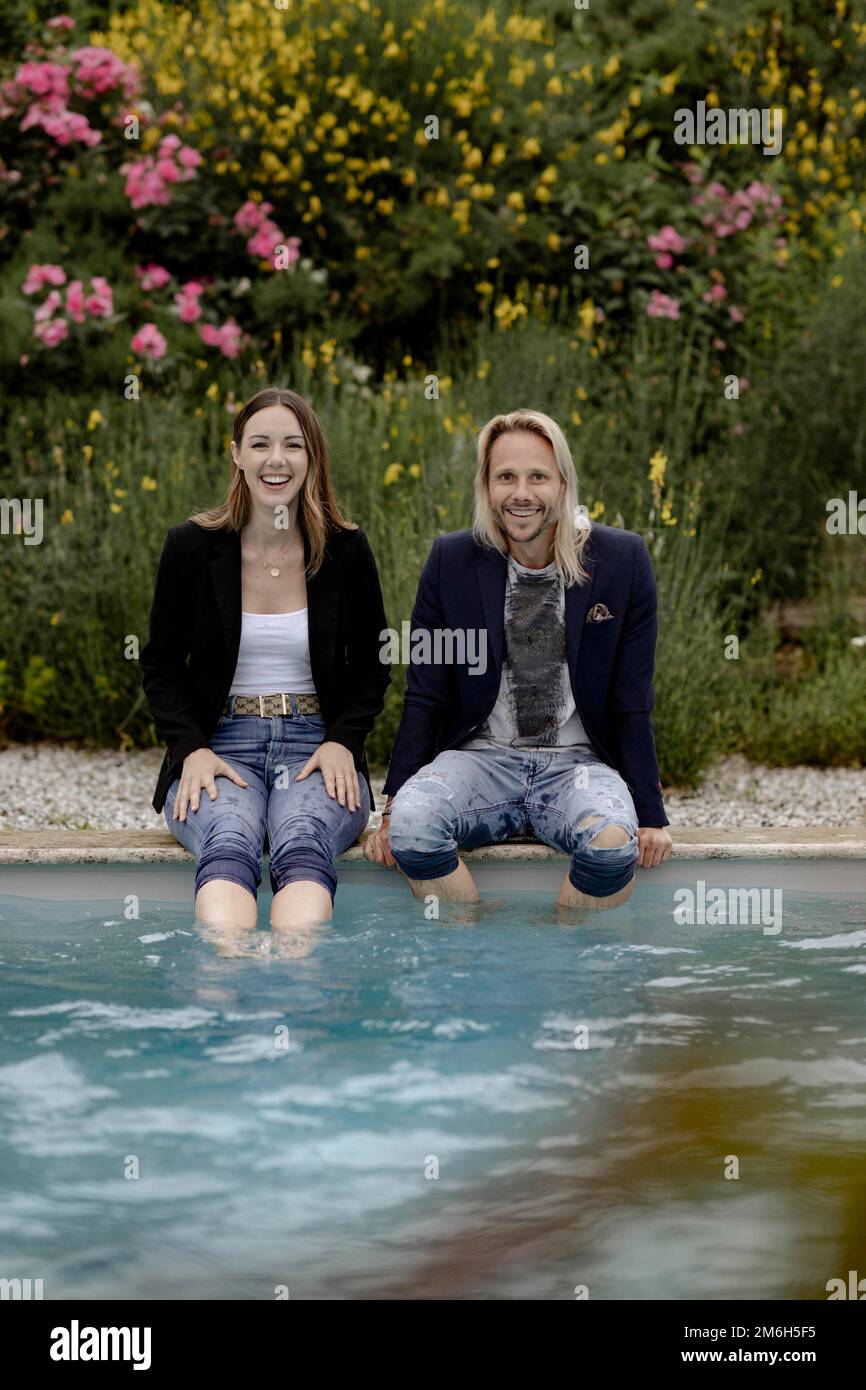 Ein lachendes Paar, das am Pool sitzt Stockfoto