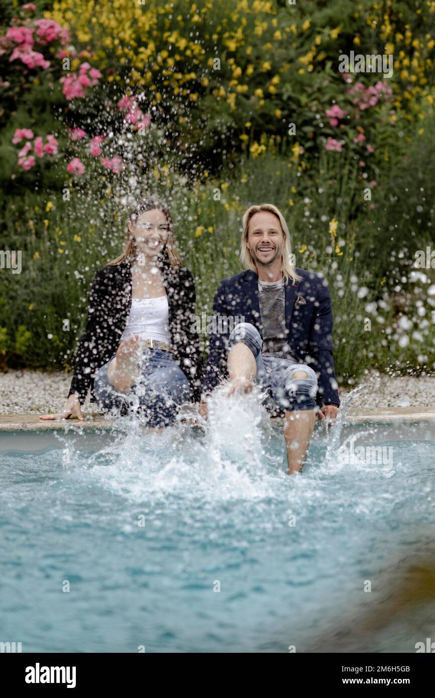 Ein Paar sitzt am Rand des Pools und spritzt Wasser Stockfoto