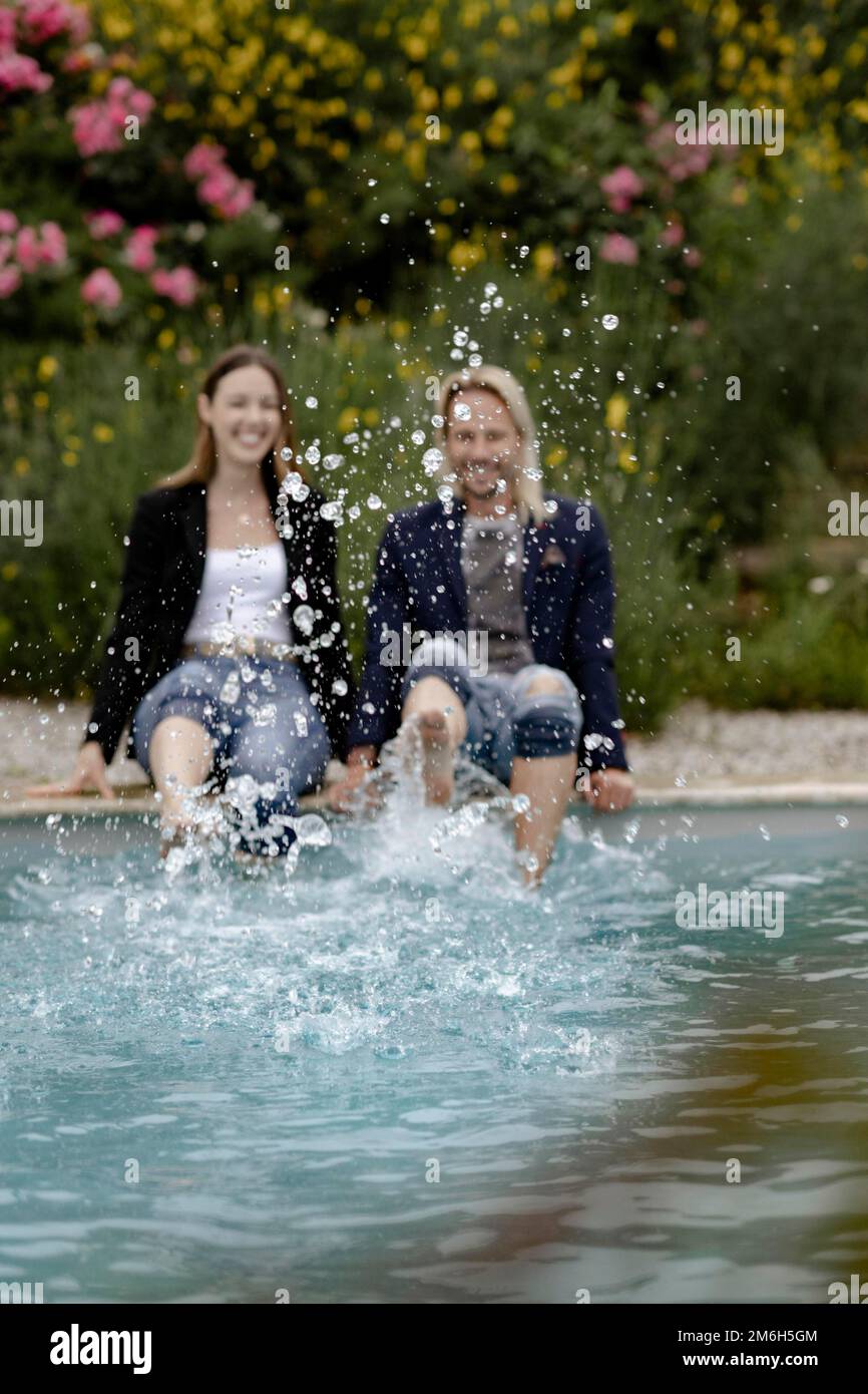 Ein Paar sitzt am Rand des Pools und spritzt Wasser Stockfoto