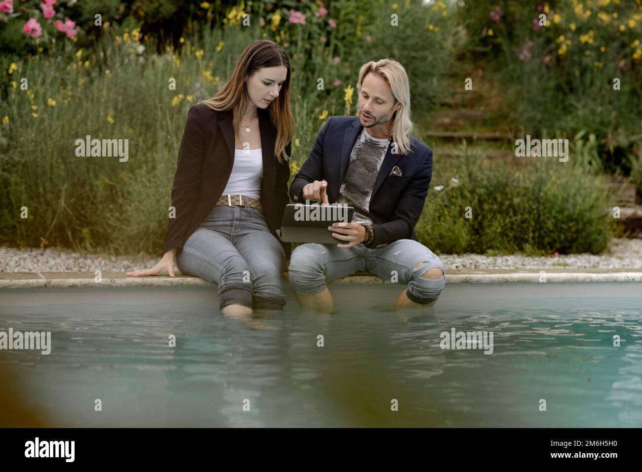 Mann und Frau mit Laptop sitzen am Pool Stockfoto