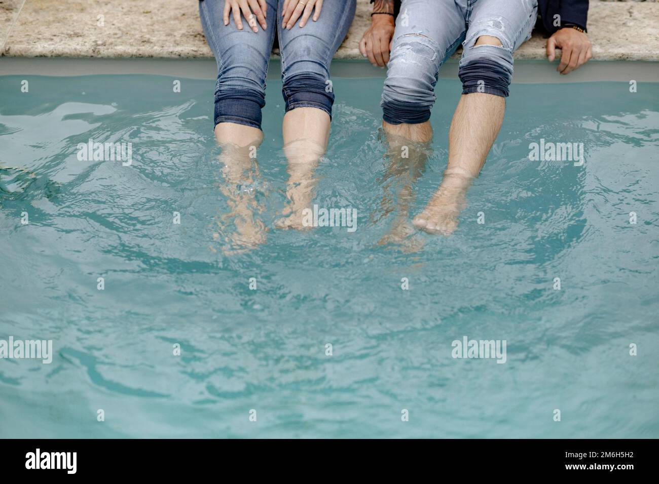 Vier Beine in Jeans im Swimmingpool Stockfoto