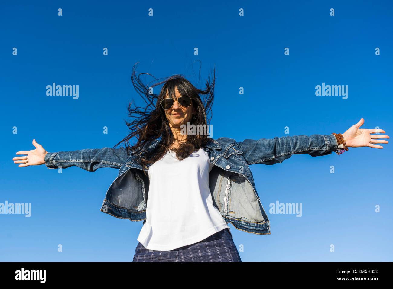 Blick aus dem niedrigen Winkel auf eine Frau, die sich ähnelt, mit offenen Armen im Freien. Blauer Himmelshintergrund Stockfoto