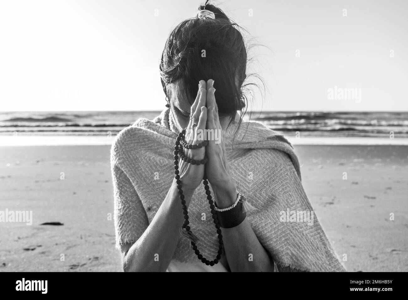 Porträt einer Frau, die sich die Hände zusammenschlägt, während sie am Strand eine japa mala hält. Namaste-Pose Stockfoto