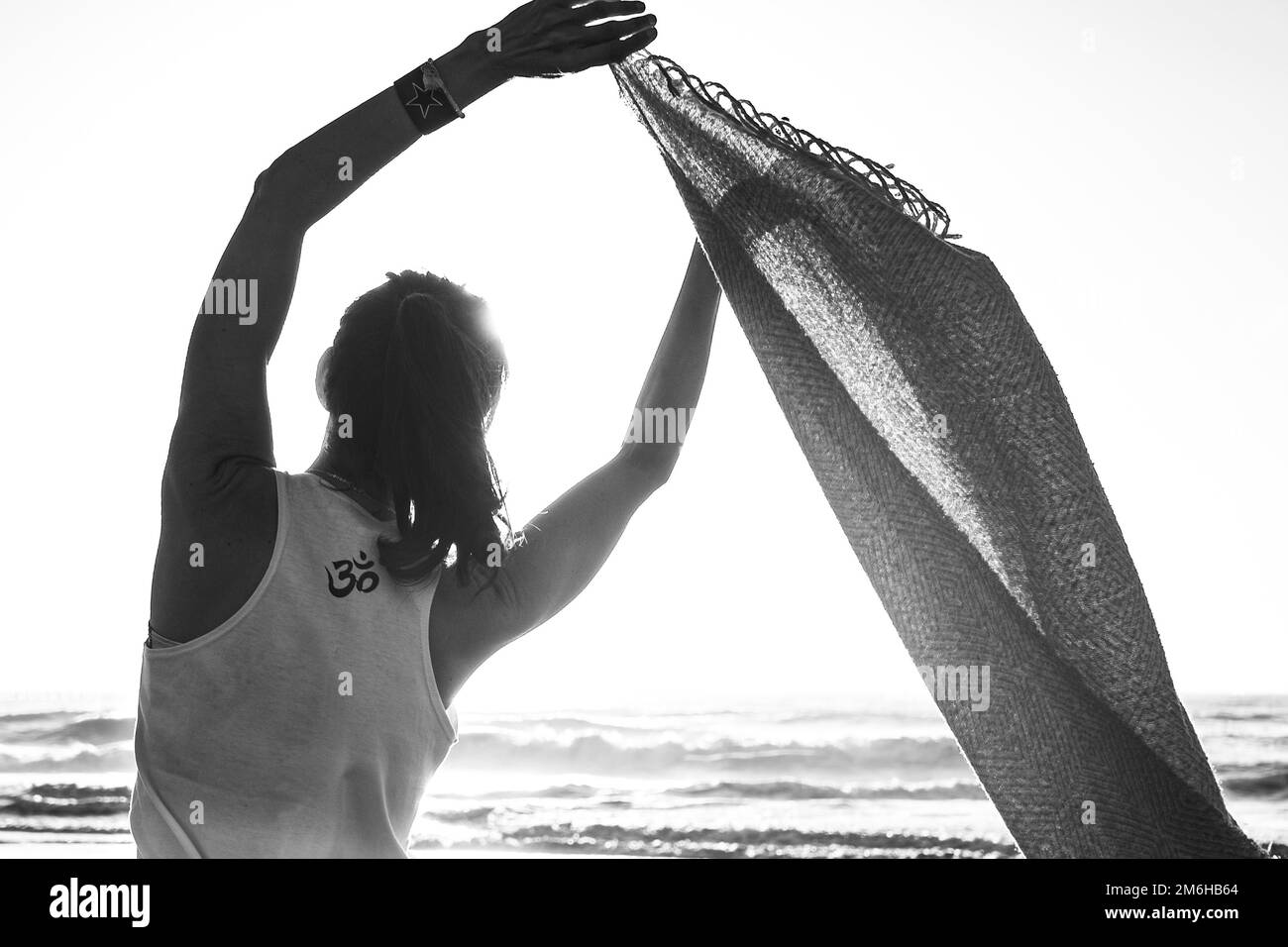 Rückansicht einer jungen Frau mit einem T-Shirt, bedruckt mit einem OM-Schild am Strand. Schwarzweißfotografie Stockfoto