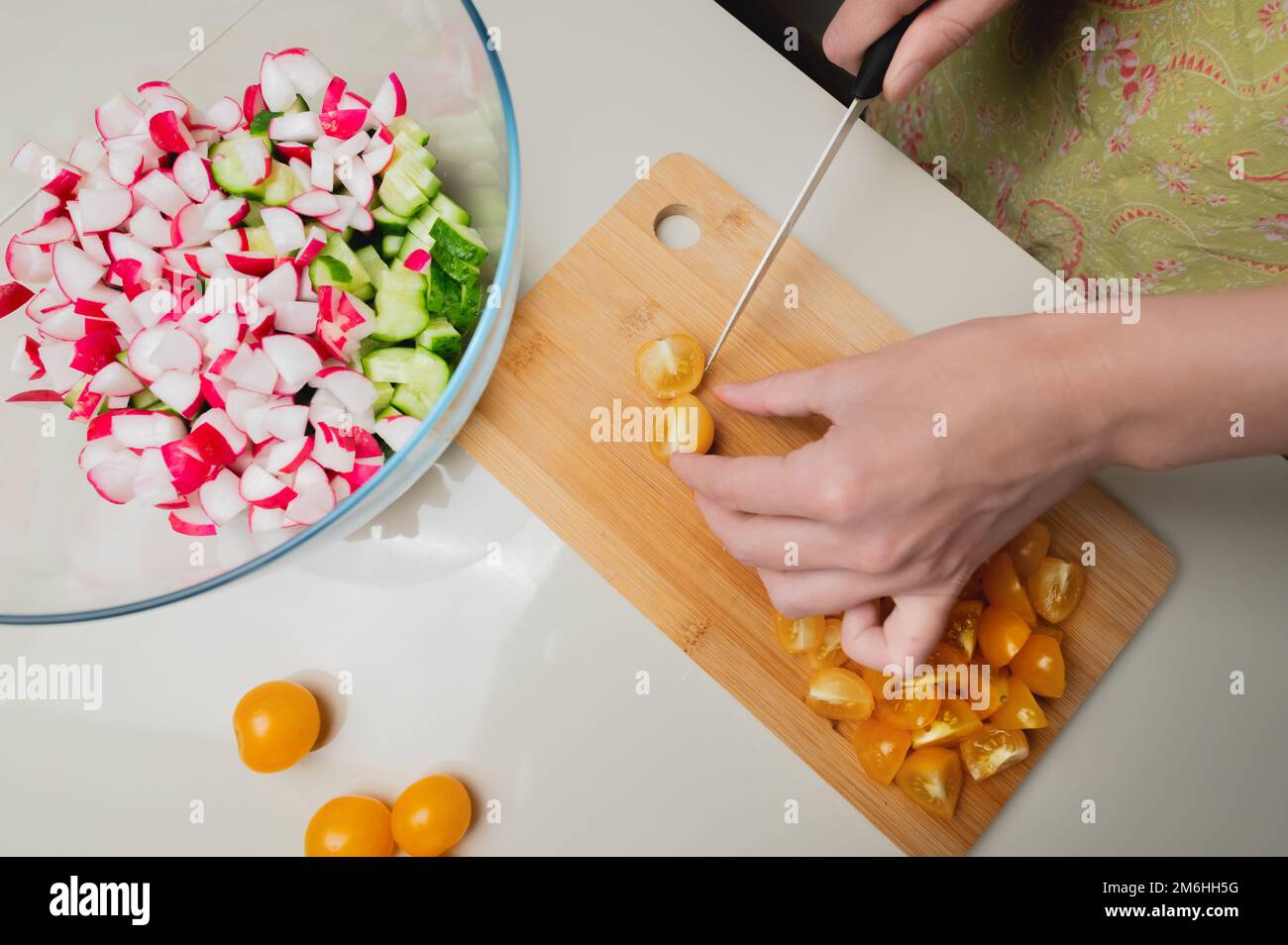 Nahaufnahme von weiblichen Händen, die Kirschtomaten für einen veganen Salat schneiden. Hausmannskost gesunde und gesunde Lebensmittel Stockfoto